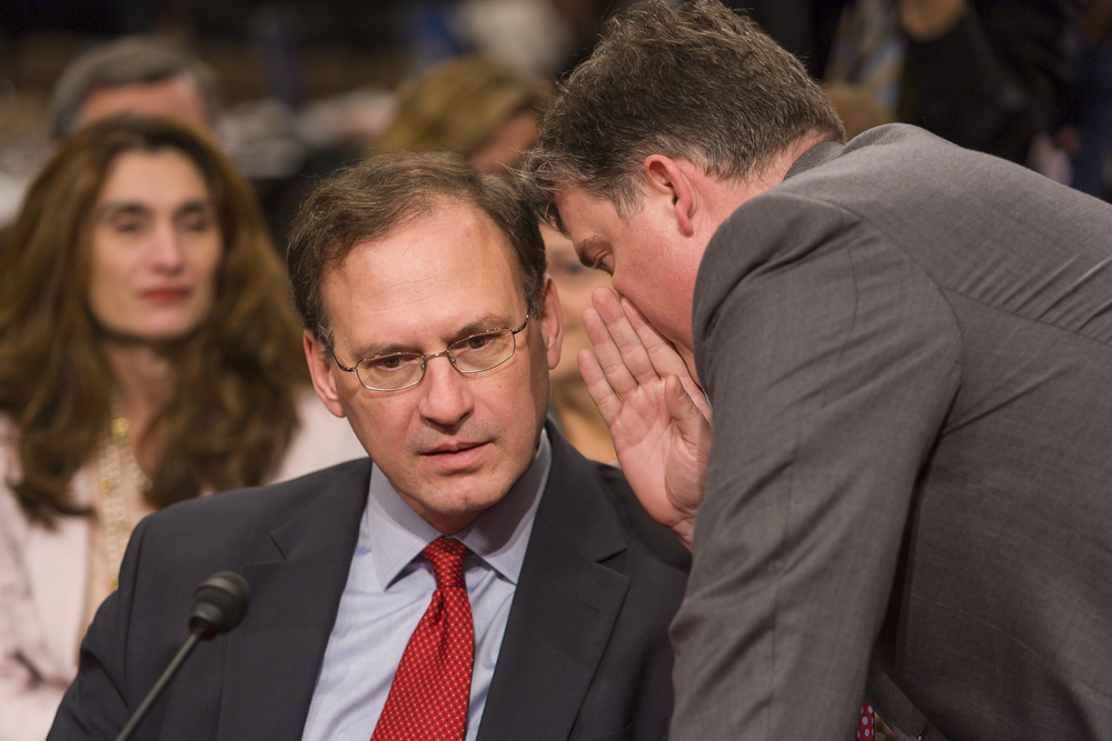 Justice Alito being whispered to at his confirmation hearing.