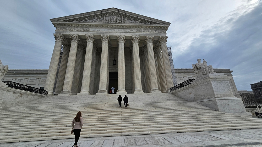 The Supreme Court building looms over the individuals climbing its stairs.