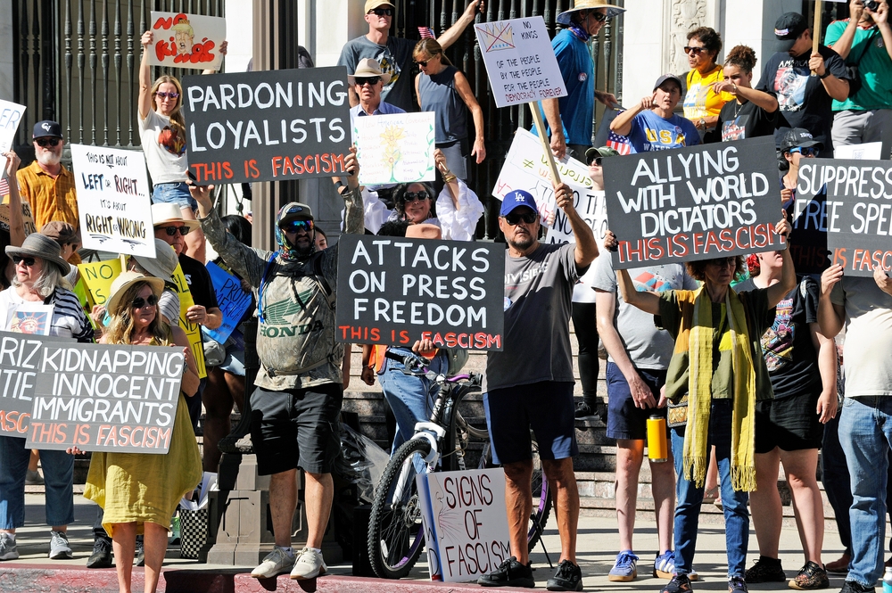 Signs from a No Kings protest indicating different Trump behaviors are examples of fascism, including kidnapping innocent immigrants, pardoning loyalists, attacking press freedom, allying with world dictators, and suppressing free speech.